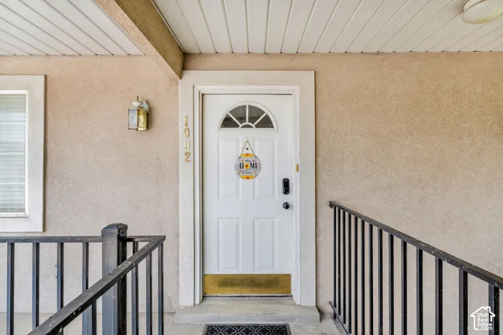 Front entry featuring a paneled door with an arched window, stucco siding, and a covered porch with a slatted ceiling