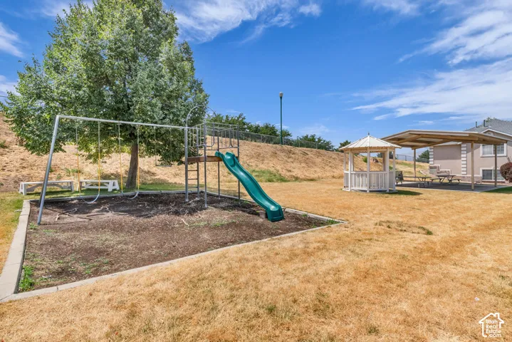 Outdoor recreational area featuring a swing set, slide, shaded gazebo, and covered patio with picnic tables