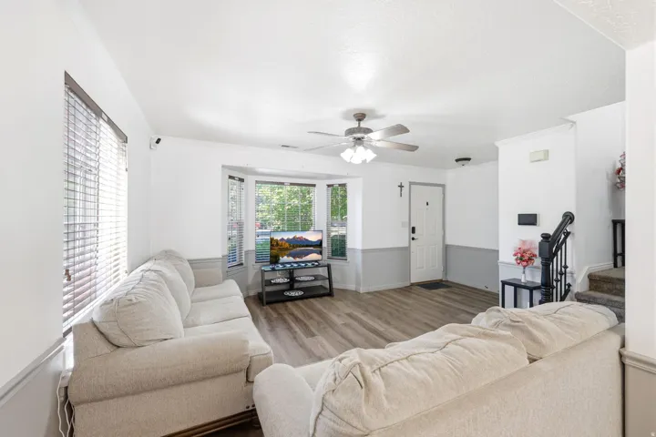 Spacious living area featuring wood-finish flooring, a bay window, and a ceiling fan with integrated lighting