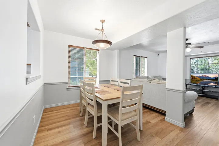 Dining area featuring wood-finish flooring, a contemporary chandelier, a window with horizontal blinds, a pass-through opening to the left, and a half-wall partition