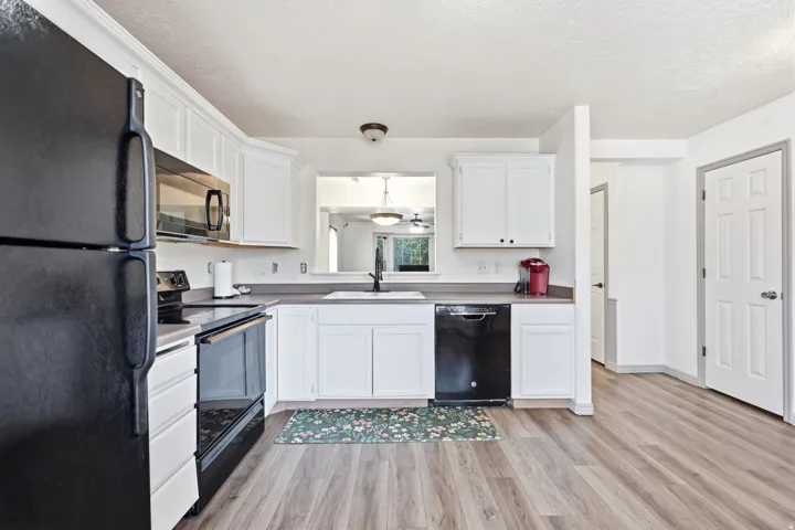 Kitchen featuring white cabinetry, wood-finish flooring, dark countertops, and a black appliance suite including a refrigerator, range, and dishwasher