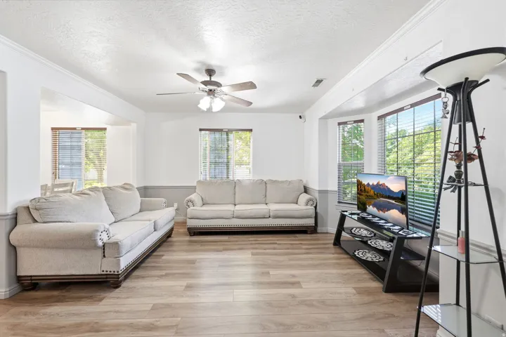 Living area featuring wood-finish flooring, a ceiling fan, crown molding, and a bay window