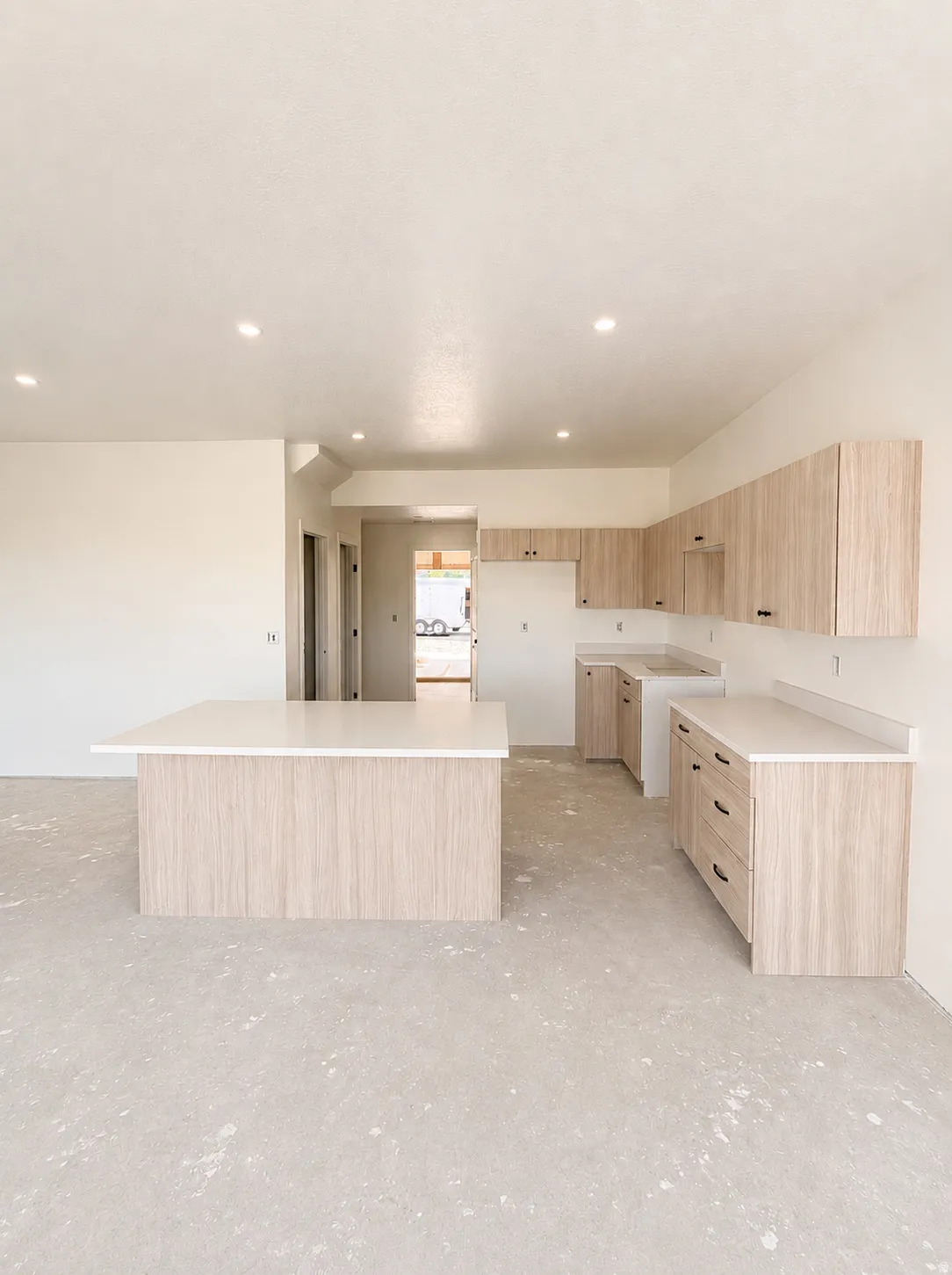 Spacious kitchen featuring light wood-finish cabinetry, a large center island with waterfall countertop, white quartz countersurfaces, stainless steel appliances, and recessed ceiling lighting throughout the open layout