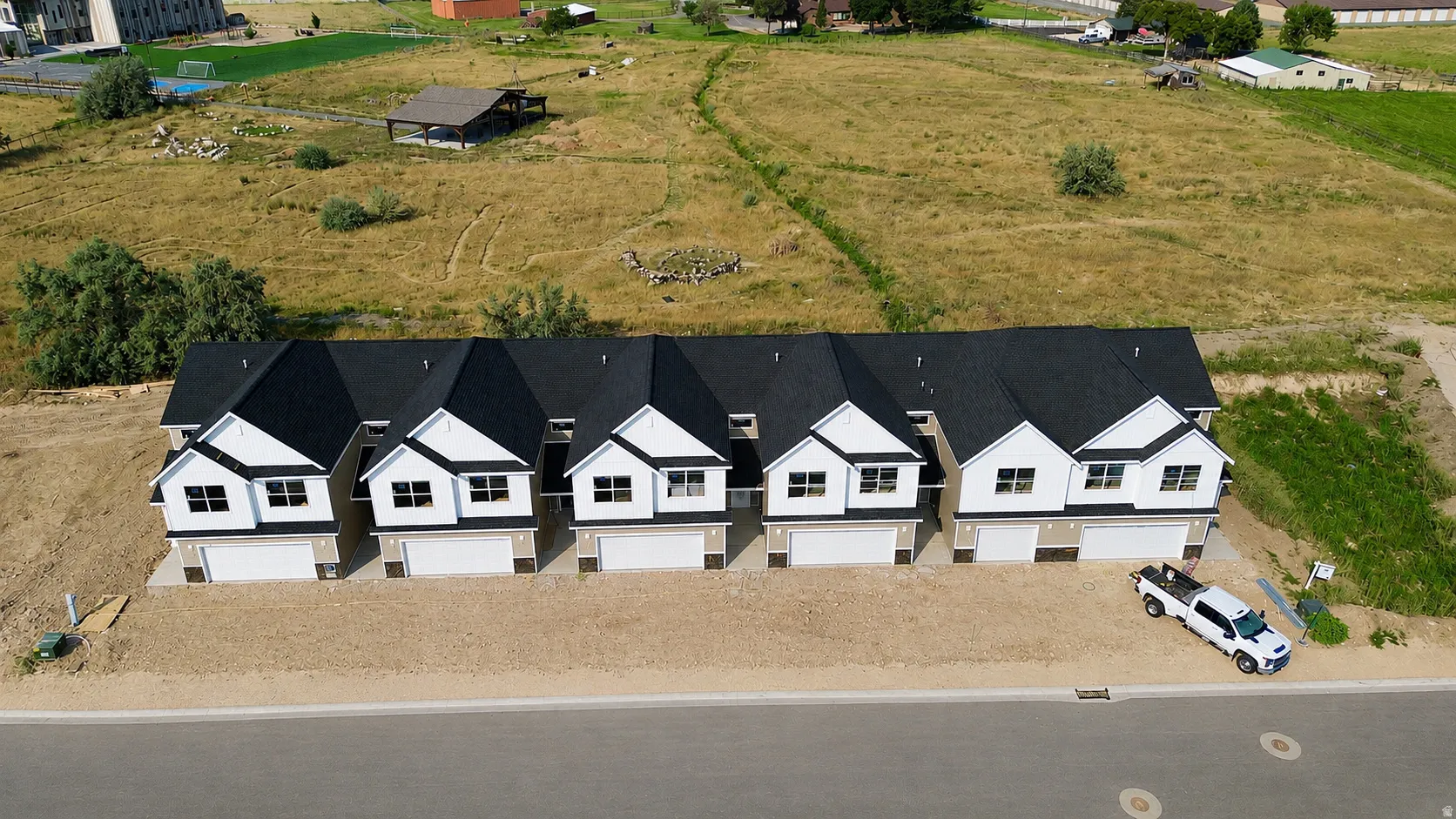 Row of newly constructed townhomes featuring dark shingle roofs, white siding, and attached garages