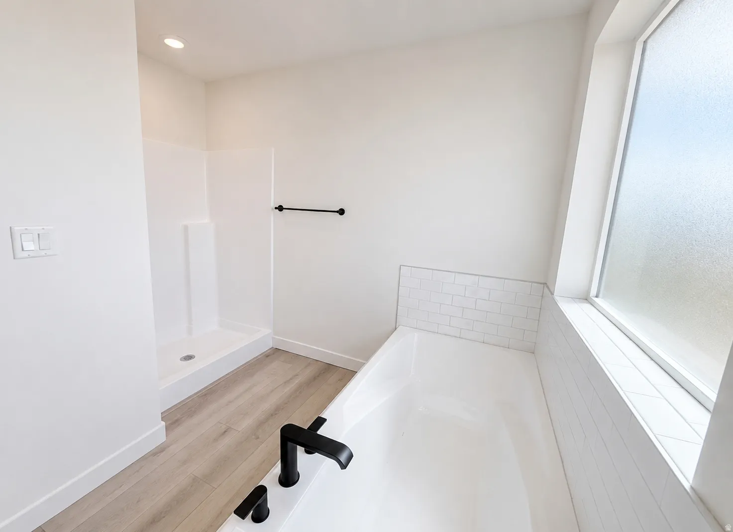 White bathtub with black fixtures, subway tile surround, and a frosted window
