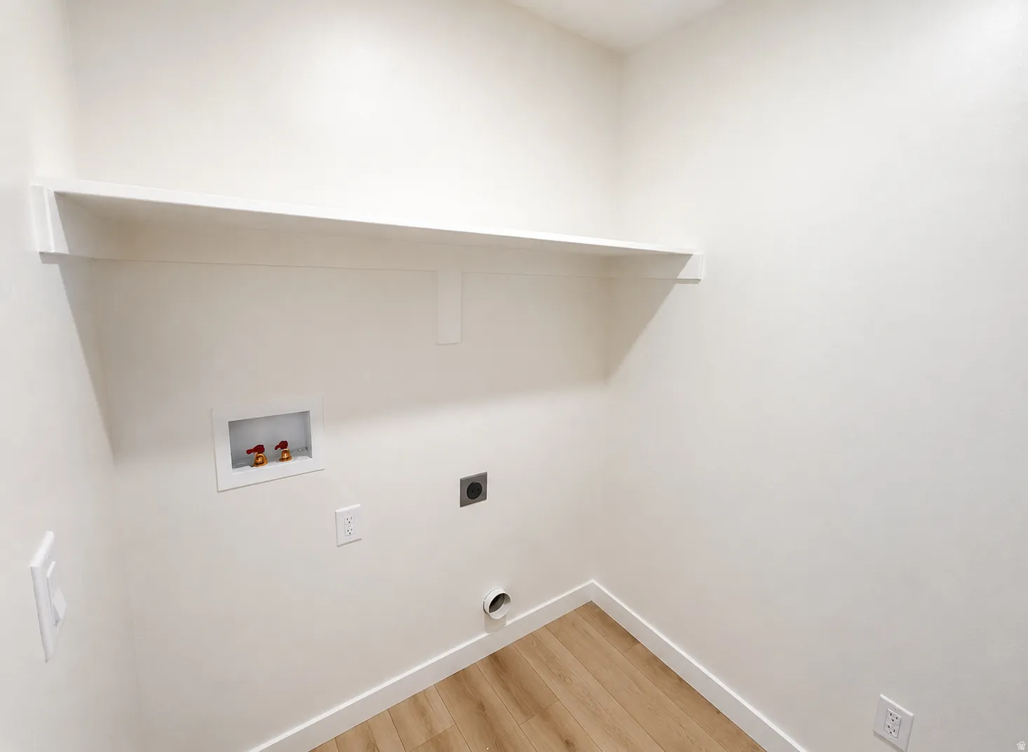 Built-in shelving with wood-finish flooring, white walls, and dedicated utility hookups