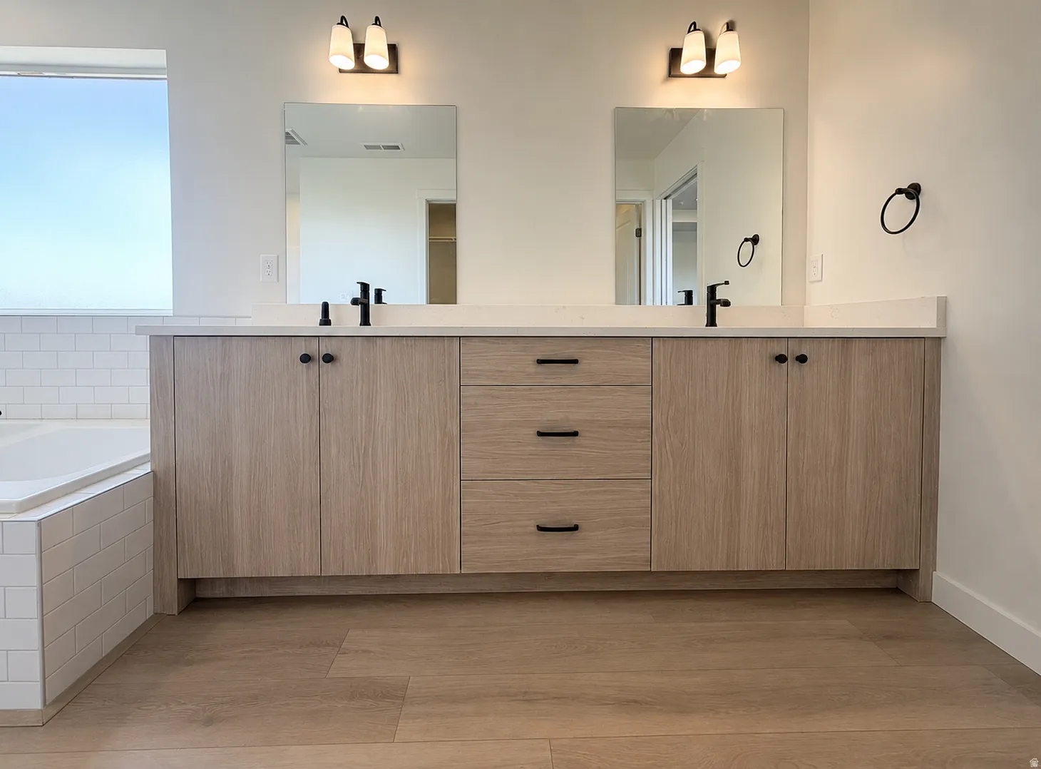 Double vanity with light wood-finish cabinetry, white countertops, and matte black fixtures