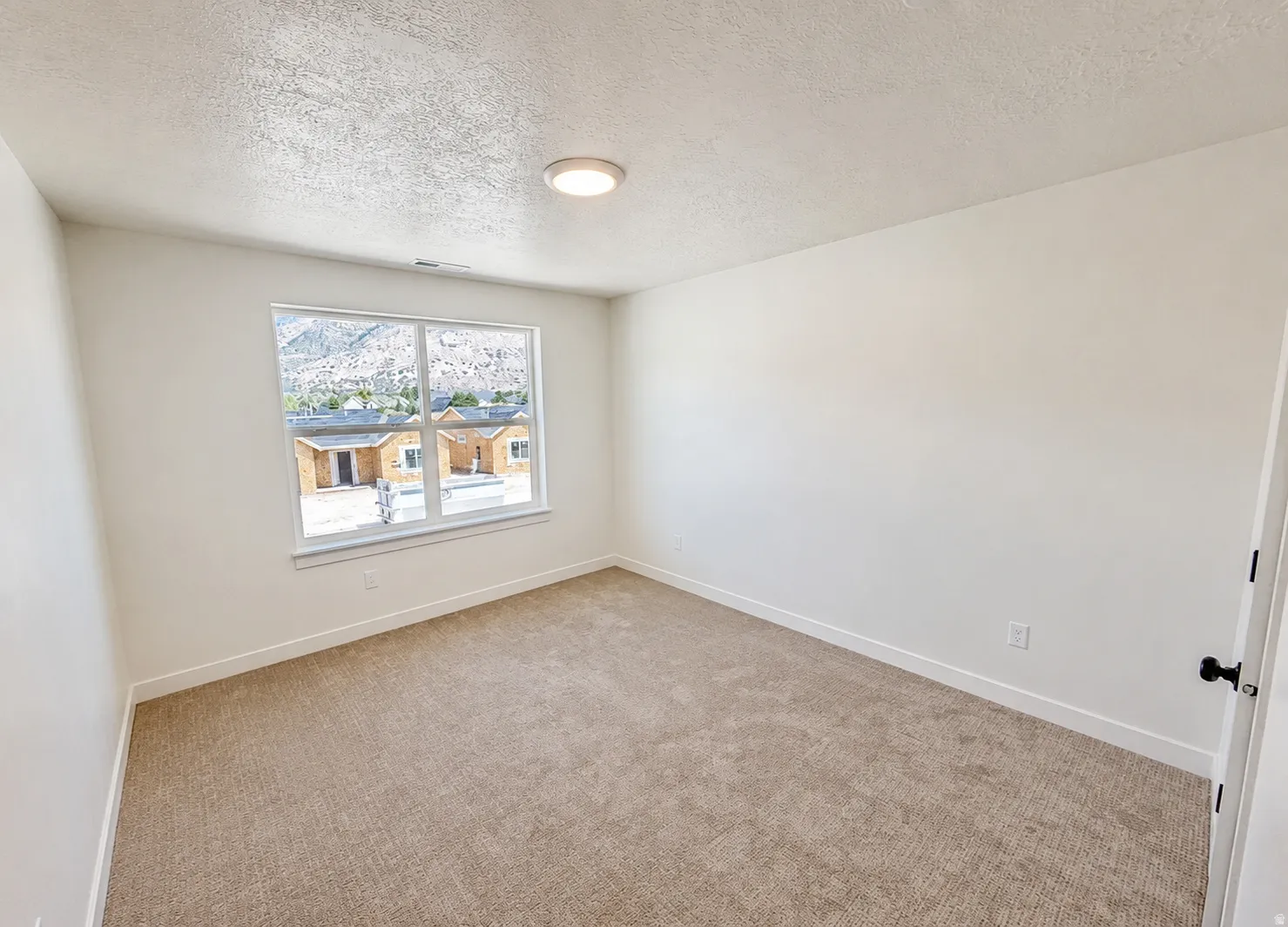 Neutral tone carpeting, white painted walls, flush mount ceiling light fixture, white trim, and a window with mountain scenery