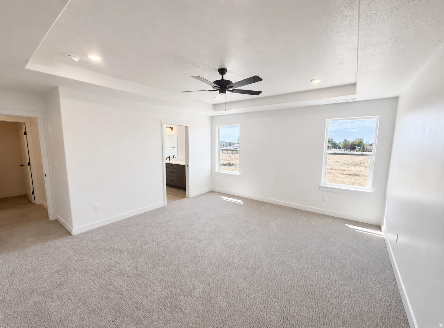 Spacious room featuring a tray ceiling with recessed lighting, a ceiling fan, two windows, and neutral carpeting