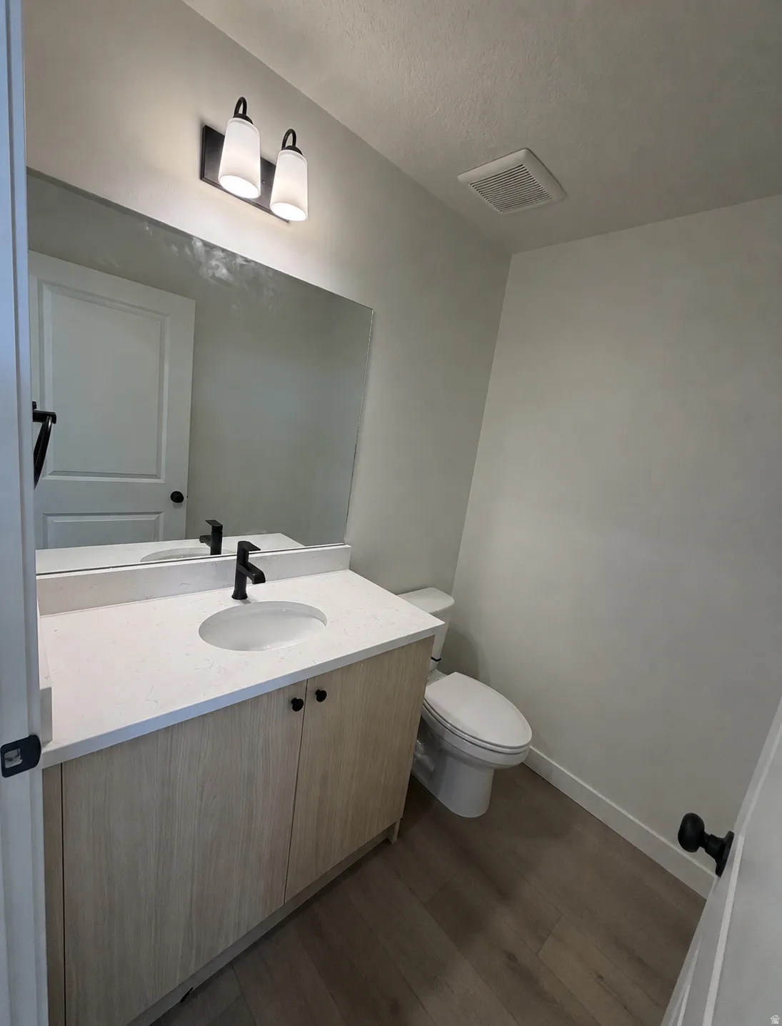 Vanity with a light-toned wood-finish cabinet, integrated sink, and white countertop