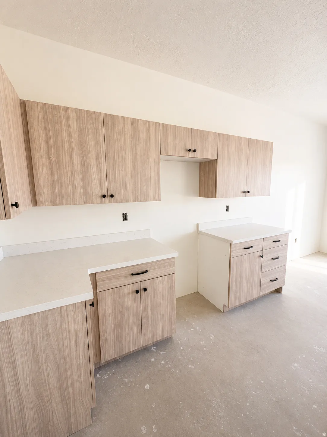 Wood-finish cabinetry with matte black hardware, light-toned countertops, and a clean, neutral wall finish