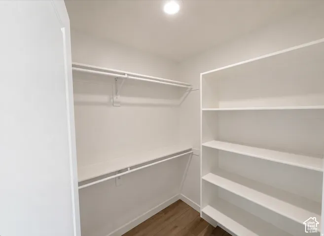 Walk-in closet featuring built-in shelving, two hanging rods, and wood-finish flooring