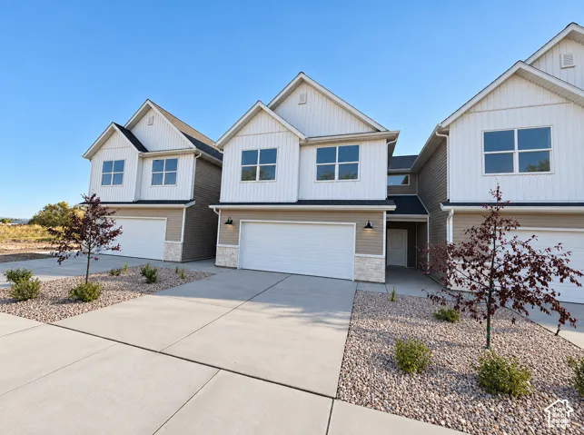 Modern townhome exterior featuring vertical and horizontal siding, stone accents, two-car garage, and concrete driveway