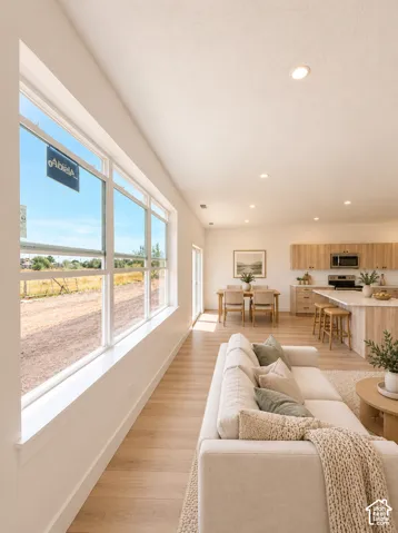 Expansive window offering abundant natural light, wood-finish flooring throughout, recessed ceiling lighting, and a kitchen featuring a central island with bar seating and light wood cabinetry