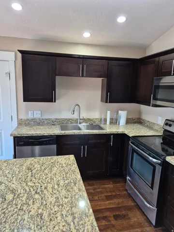 Kitchen featuring dark wood cabinetry, granite-finish countertops, stainless steel appliances, and wood-finish flooring