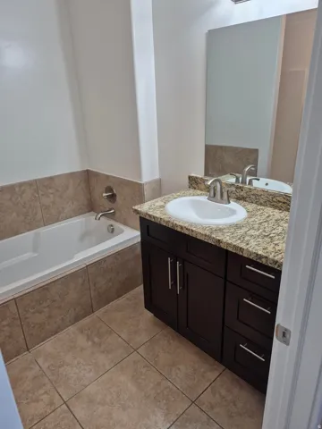Bathroom featuring a white drop-in tub, tiled surround, and a dark wood-finish vanity with a granite countertop and undermount sink