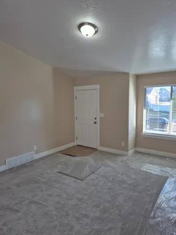 Entryway with neutral wall paint and a light fixture, featuring a paneled door, window with blinds, and carpeted flooring