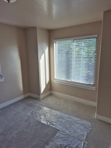 Spacious room featuring neutral paint, clean gray carpeting, white baseboards, and a large window with blinds