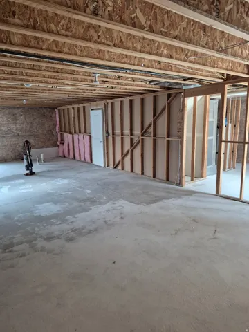 Unfinished basement with concrete flooring, exposed ceiling joists, framed interior walls, and visible insulation