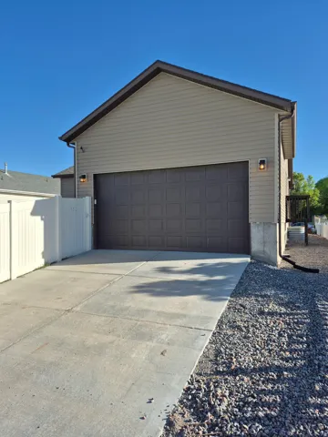 Rear-facing attached garage with a panel-style door, concrete driveway, and tan siding