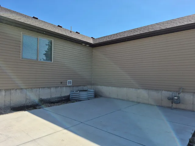 Concrete patio with a basement window well, framed by tan siding and a concrete foundation