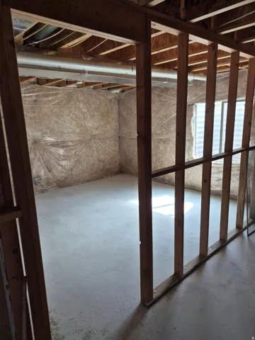 Unfinished basement space with exposed wood framing, concrete flooring, and insulated walls
