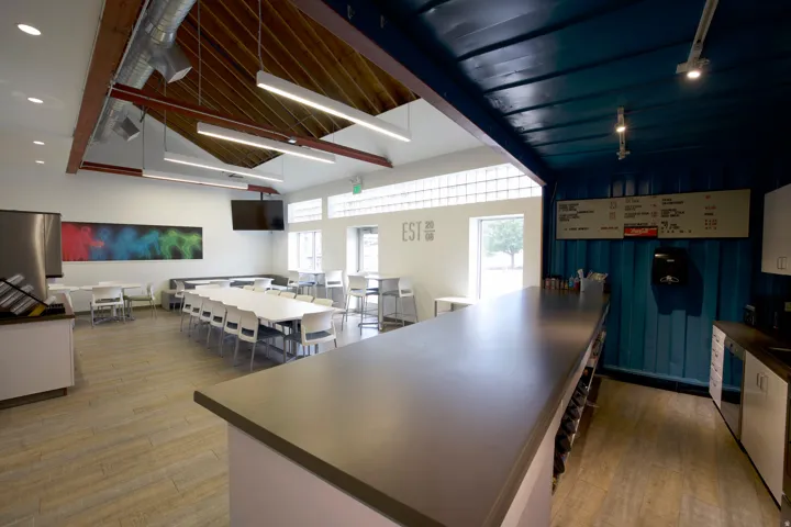 Spacious common area featuring vaulted ceilings with exposed wood beams, linear lighting fixtures, and light wood-finish flooring