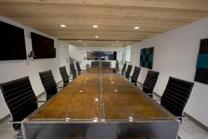 Spacious conference room featuring a large wood-finish table, a wood-paneled ceiling with recessed lighting, and multiple wall-mounted displays