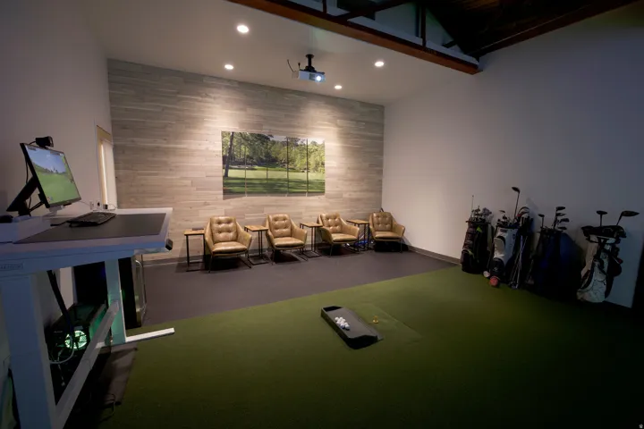 Indoor golf simulator room featuring a projector, recessed lighting, a wood-finish accent wall, and exposed ceiling beams