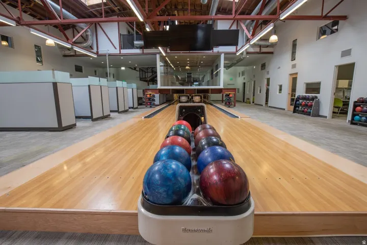 Bowling alley featuring polished wood lanes, exposed ceiling trusses, a second-level glass-enclosed space, and built-in bowling ball racks