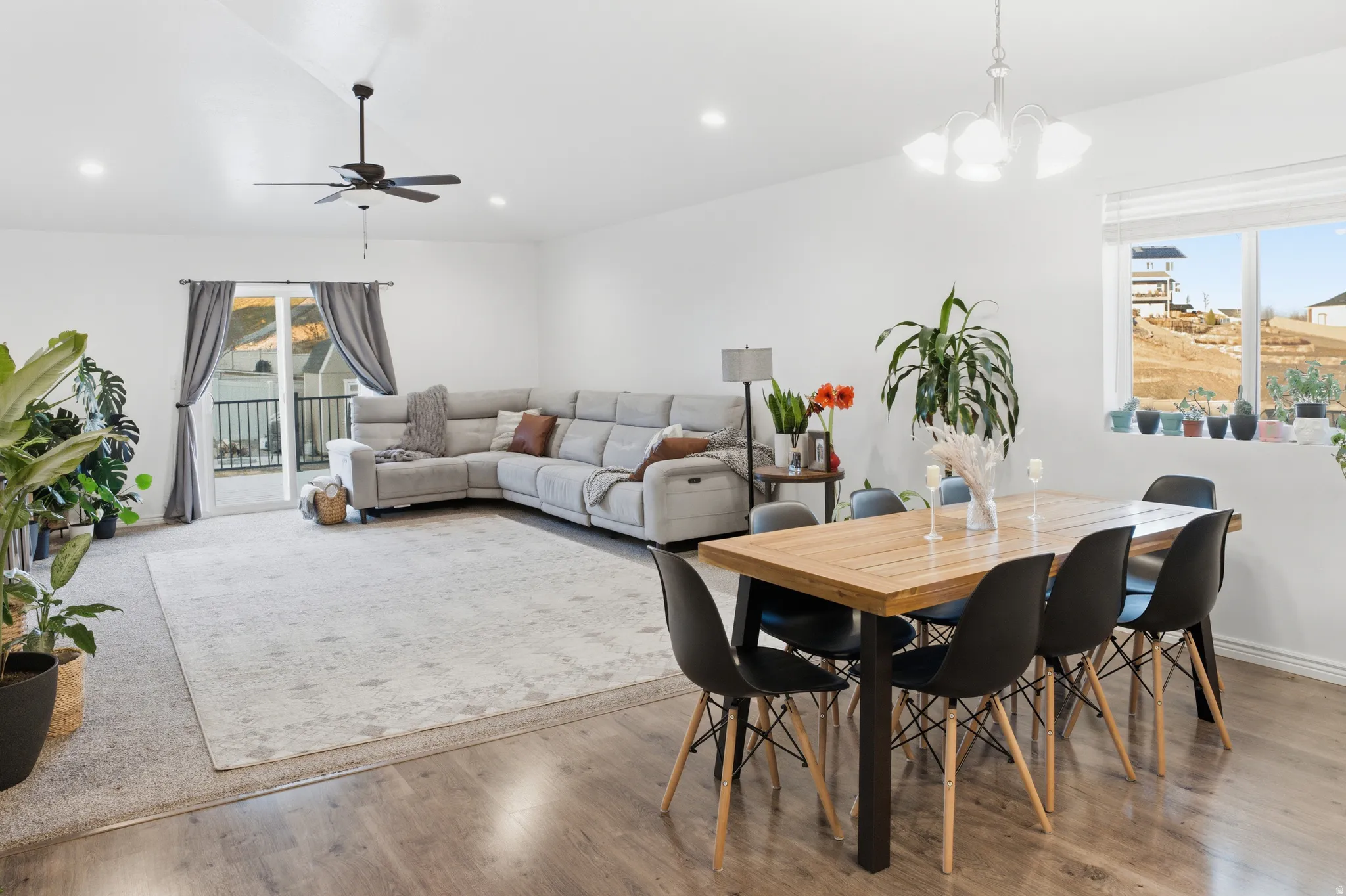 Open concept living and dining area featuring vaulted ceilings, recessed lighting, wood-finish flooring, and a sliding glass door leading to an outdoor balcony