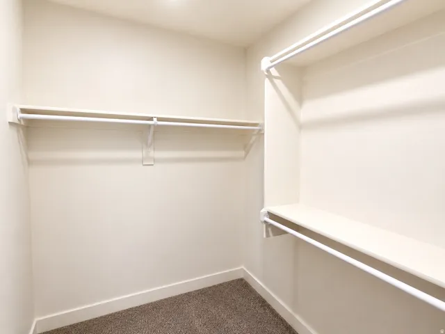 Walk-in closet with neutral-toned walls, white shelving, and hanging rods