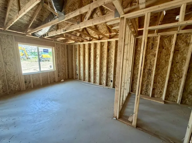 New construction framing with exposed wooden trusses, concrete slab subfloor, and a multi-pane window