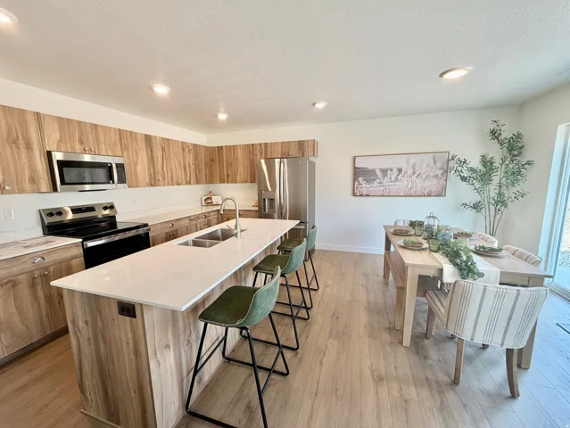 Kitchen featuring wood-finish cabinetry, stainless steel appliances, a center island with a double basin sink, and wood-finish flooring