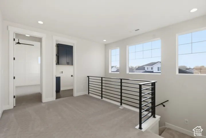 Spacious upper-level landing featuring light gray carpeting, modern black horizontal bar railing, and three large windows