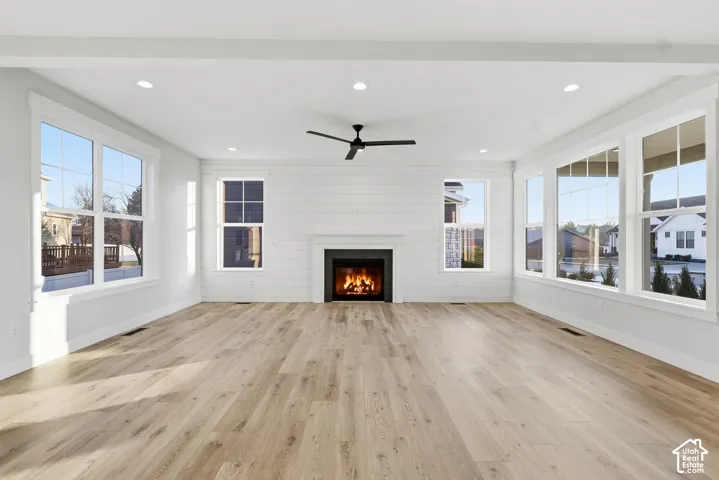 Spacious living area featuring a central fireplace with black surround and white mantel, shiplap wall detailing, expansive windows, wood-finish flooring, and a ceiling fan