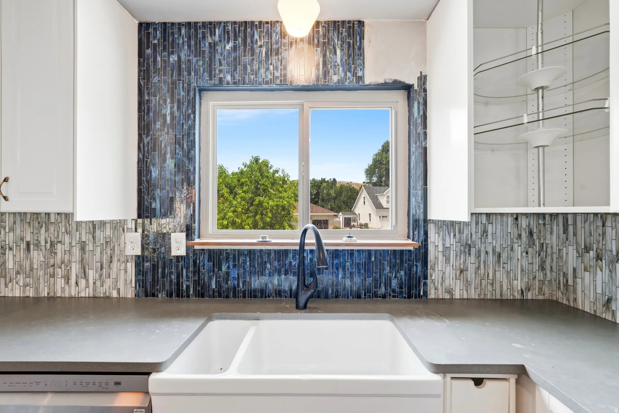 Kitchen sink area featuring a white double farmhouse sink, a black gooseneck faucet, and dark grey countertops