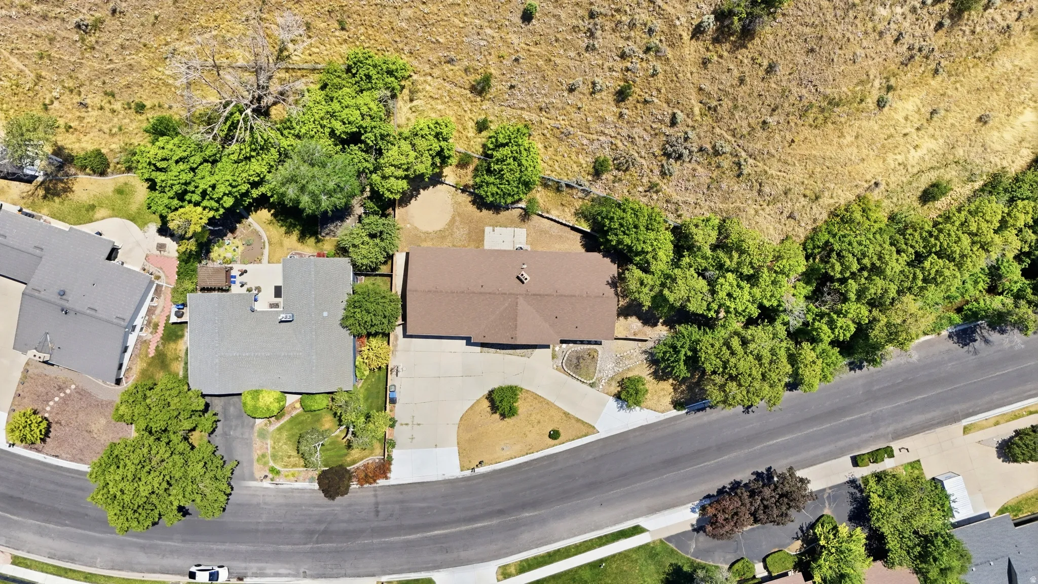 Residential property featuring a spacious lot with mature trees, a paved driveway, and a shingle roof