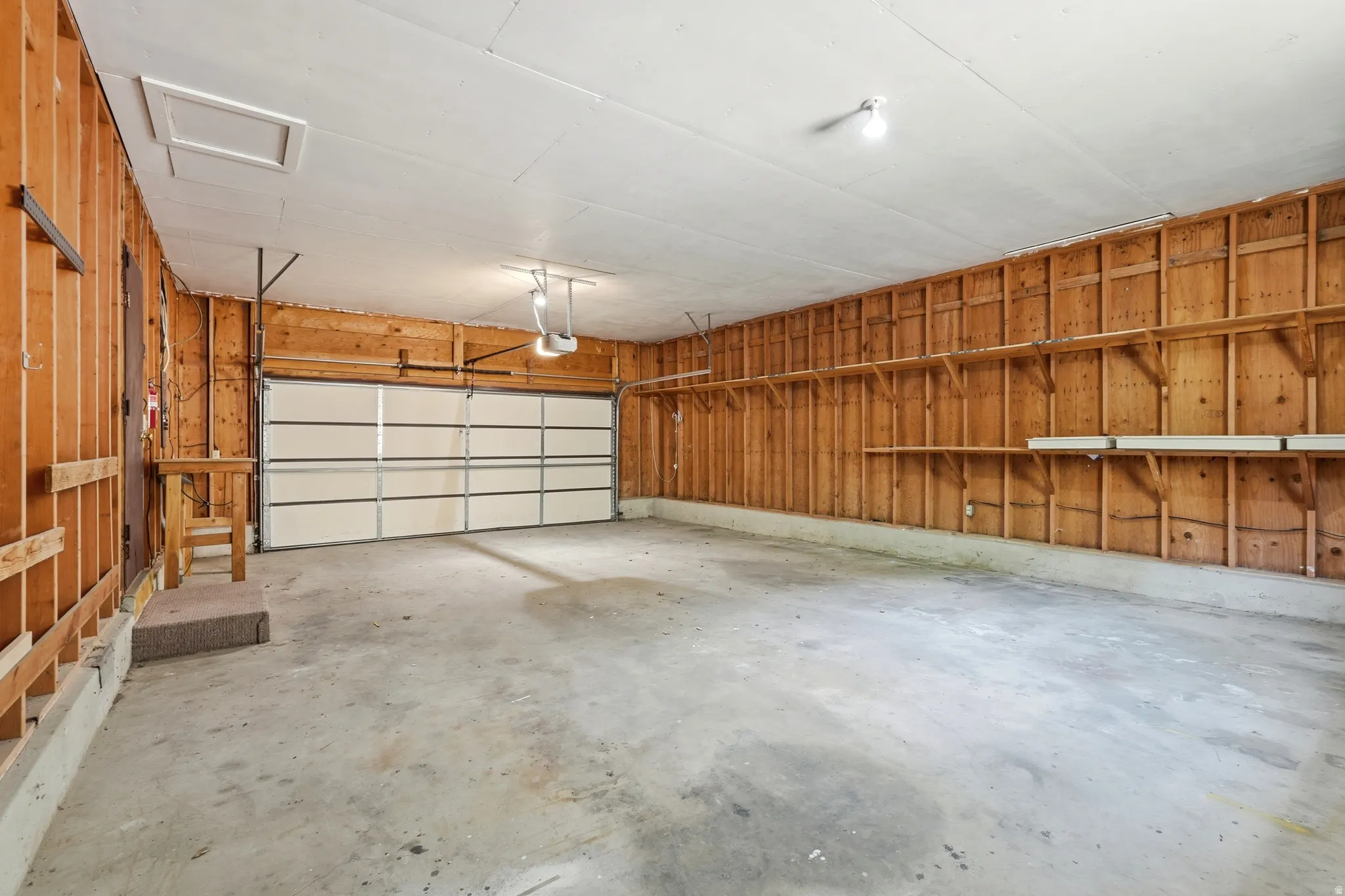 Spacious two-car garage featuring a sectional garage door, concrete flooring, exposed wood stud walls, and built-in shelving units