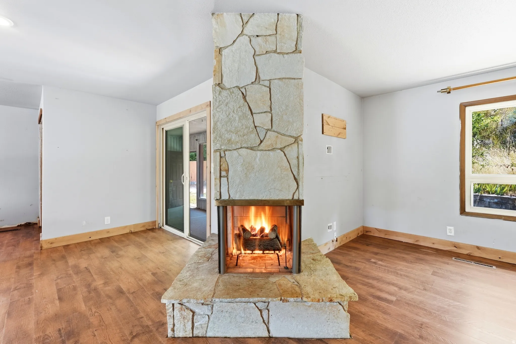 Central stone fireplace with hearth, wood-finish flooring, white walls, and a sliding glass door