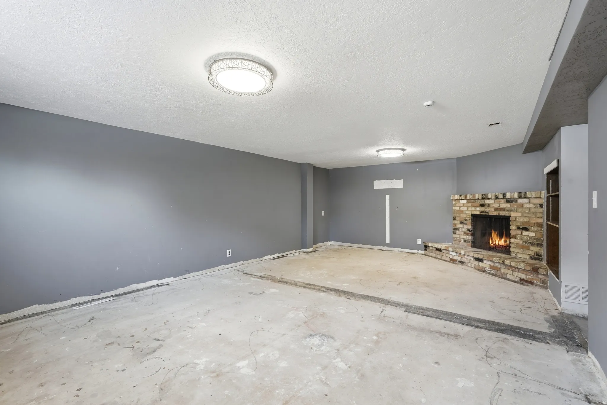 Spacious interior with an exposed concrete floor, a brick fireplace with a hearth, and modern flush-mount lighting fixtures