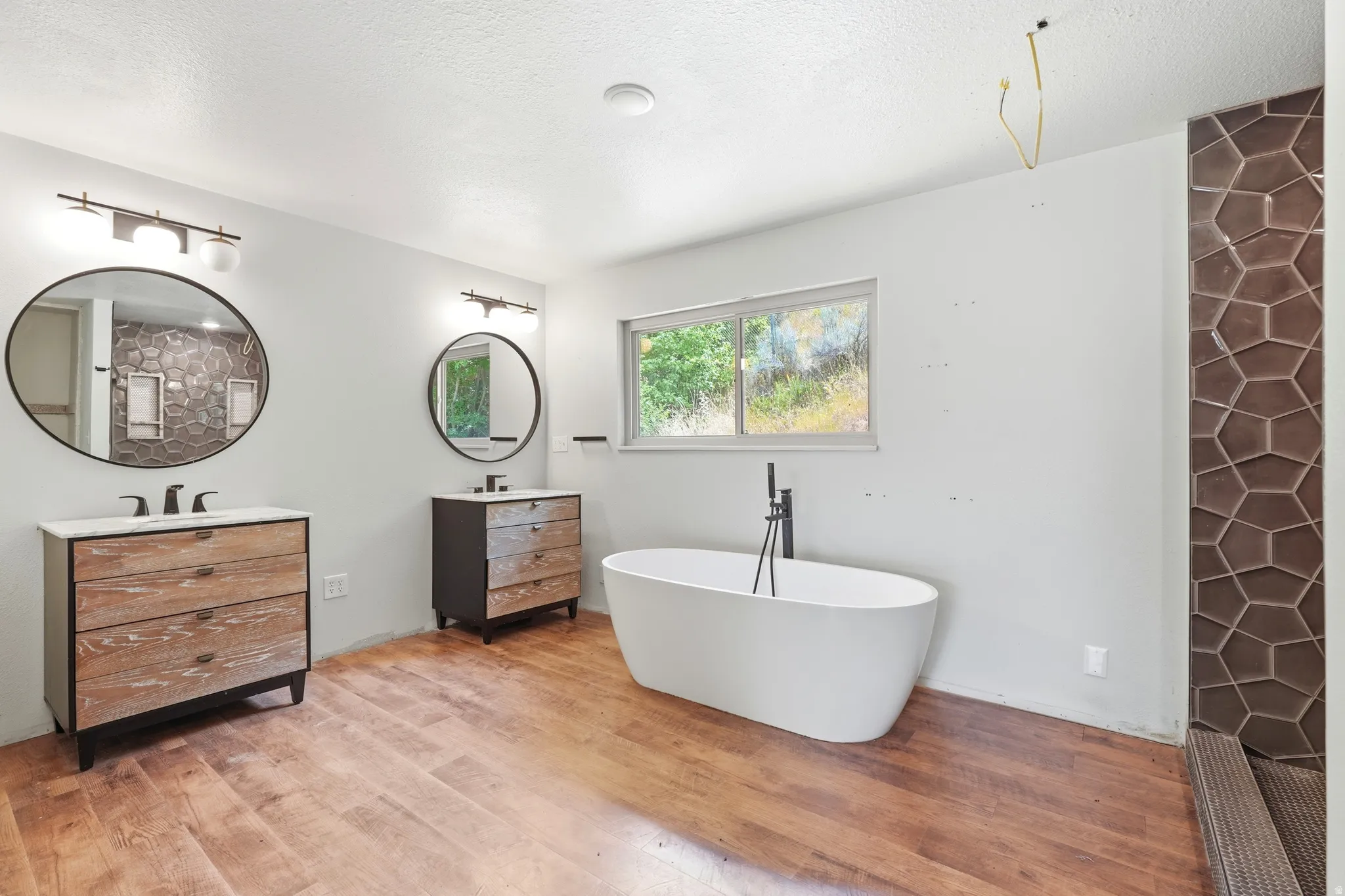 Freestanding soaking tub with a floor-mounted matte black faucet, set against wood-finish flooring