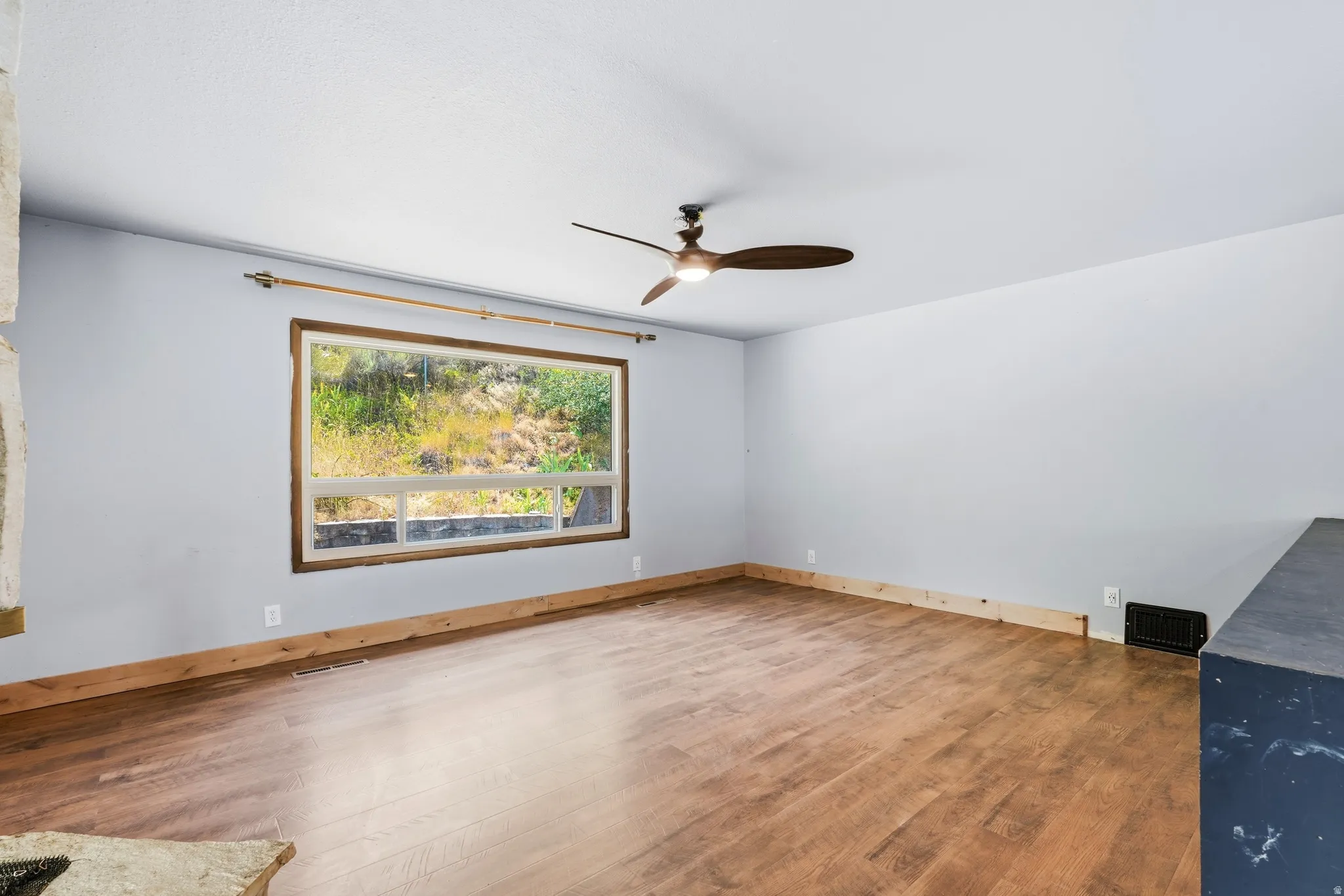 Bright room featuring wood-finish flooring, a large picture window with wooden trim, and a ceiling fan with integrated lighting