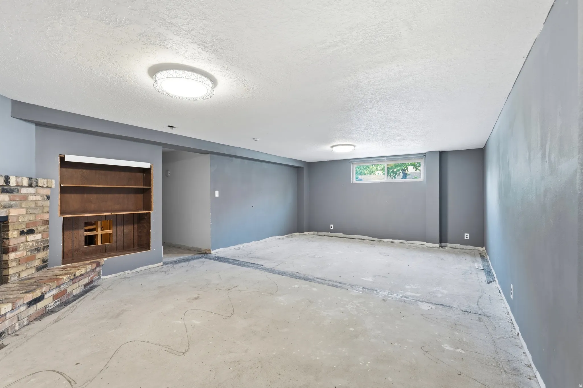 Spacious room with a brick fireplace and built-in shelving, featuring a window and recessed ceiling lights