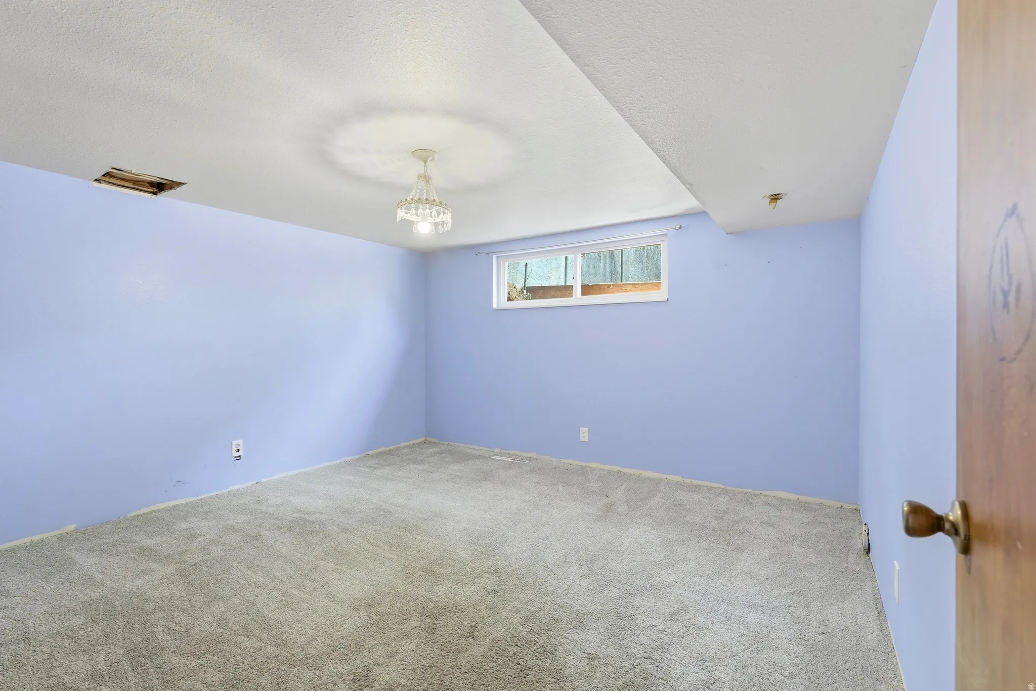 Spacious room featuring light blue walls, gray carpet, and a window with exterior visibility