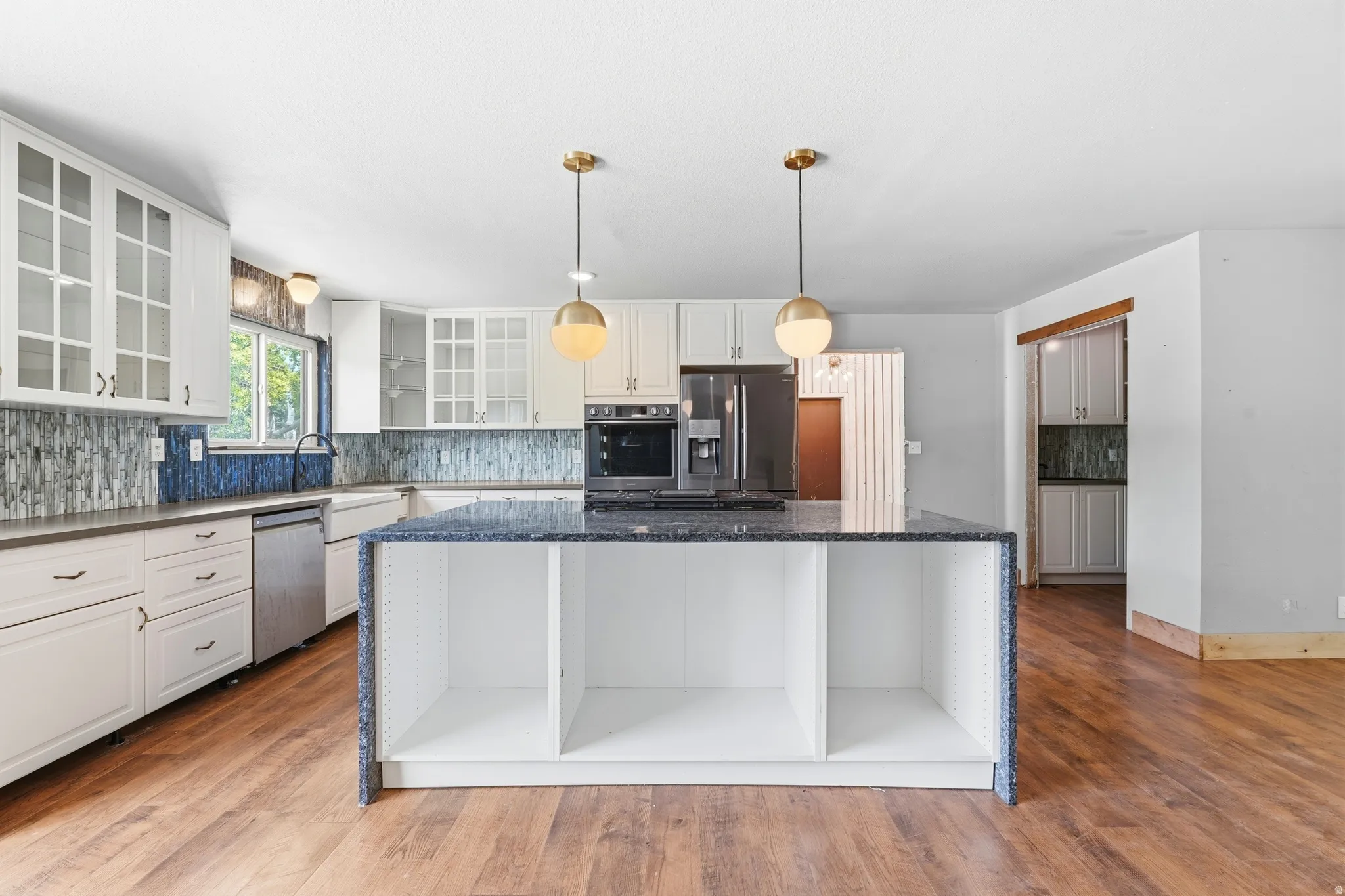 Kitchen featuring a central island with integrated shelving, granite countertops, and wood-finish flooring