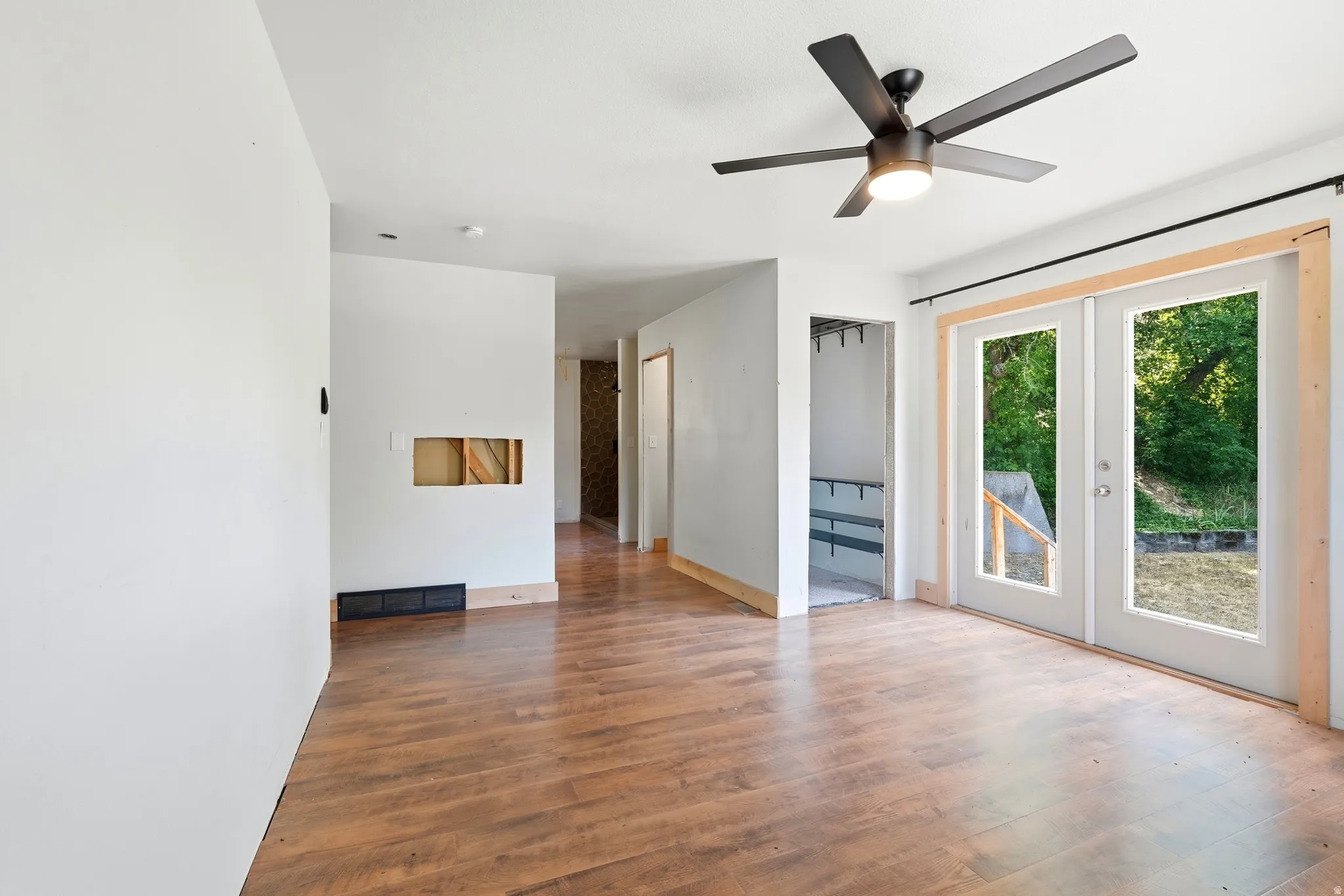 Spacious room featuring wood-finish flooring, a contemporary ceiling fan with integrated lighting, and white walls