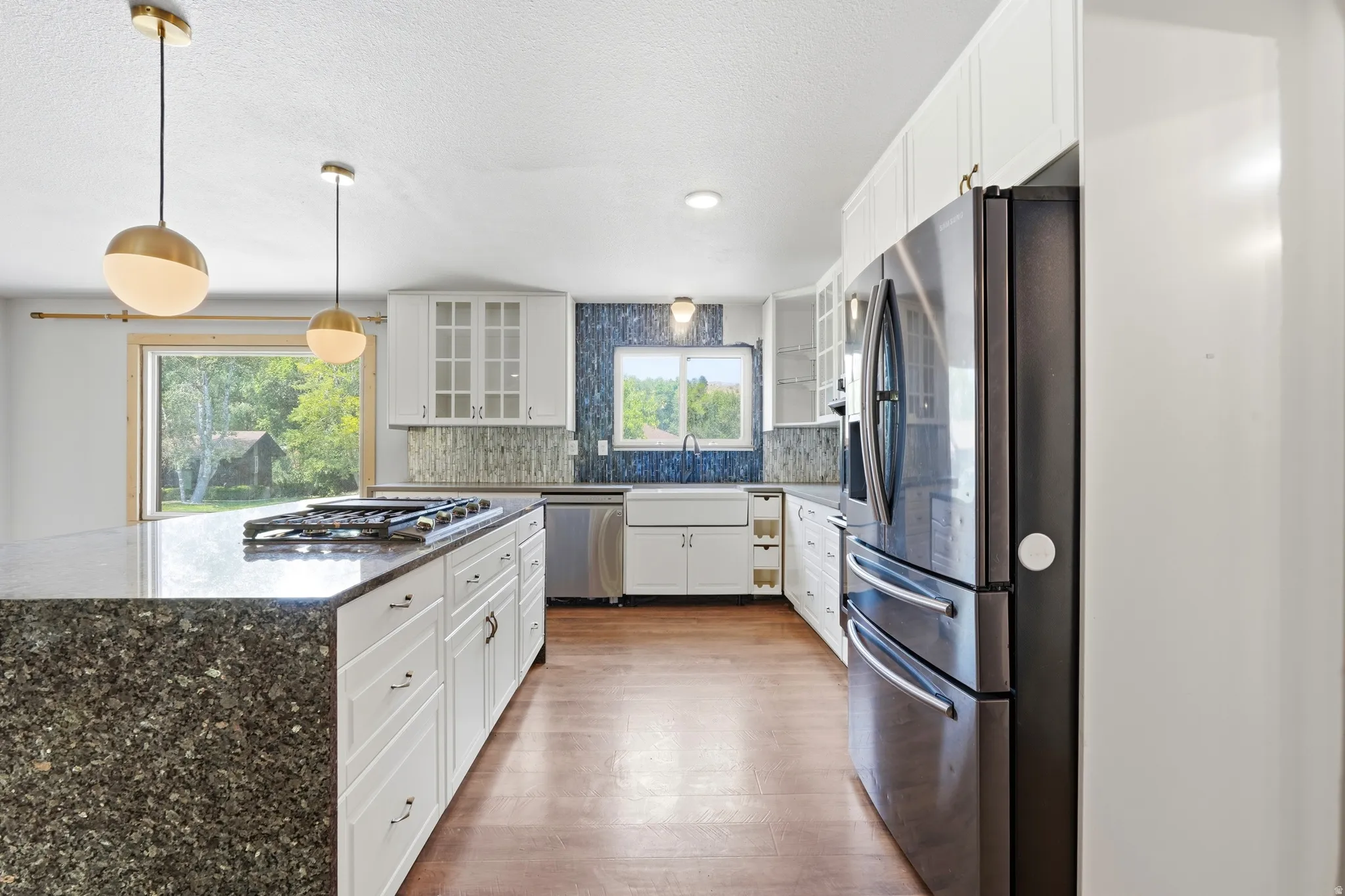 Spacious kitchen featuring a large island with a built-in gas cooktop, white shaker-style cabinetry, dark stainless steel appliances, and wood-finish flooring