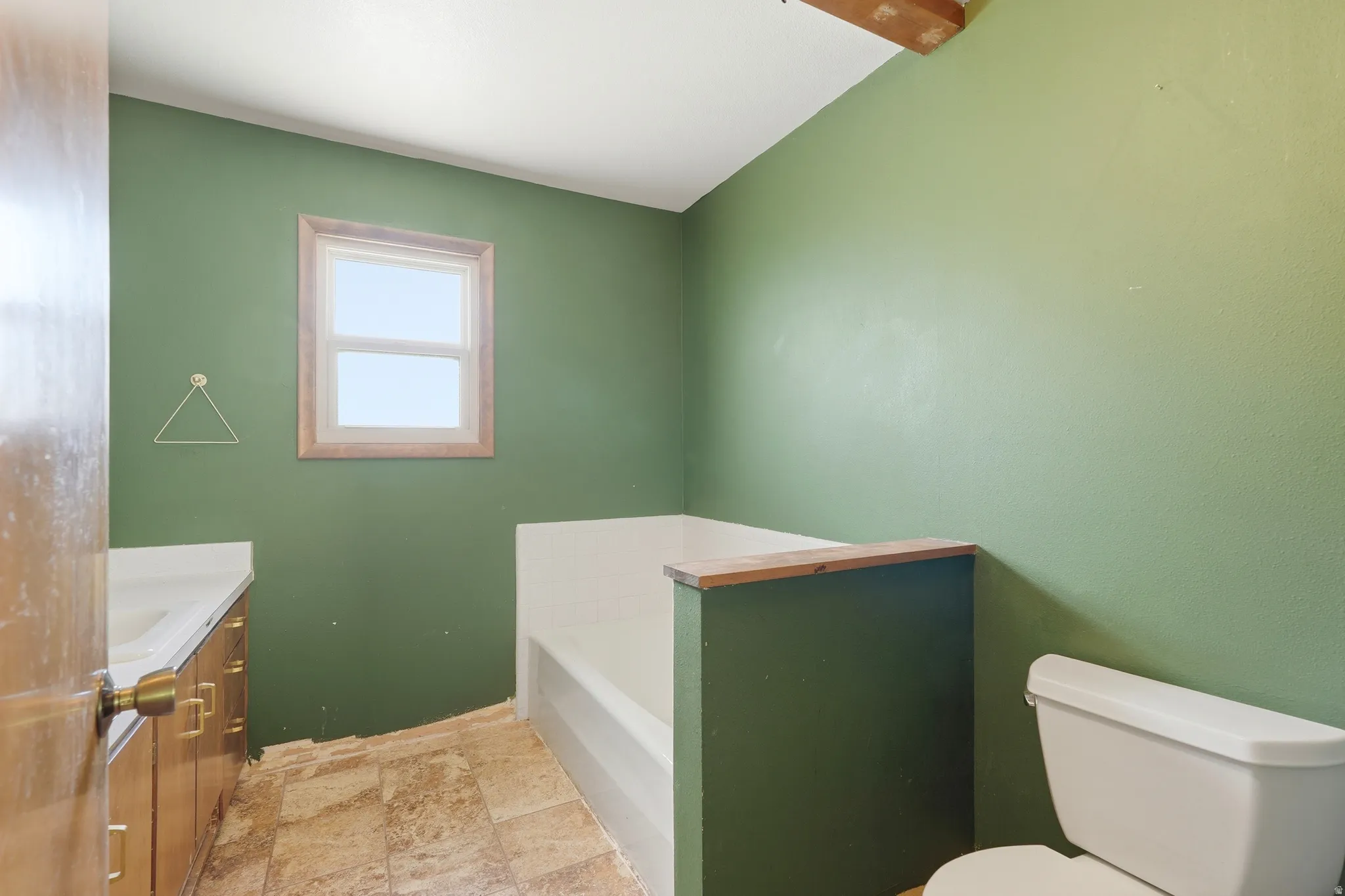 Bathroom featuring a single vanity with wood-finish cabinetry, a window with wood trim, a built-in bathtub, and a toilet