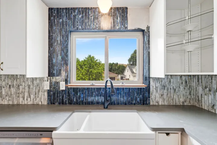 Kitchen sink area featuring a white double farmhouse sink, a black gooseneck faucet, and dark grey countertops